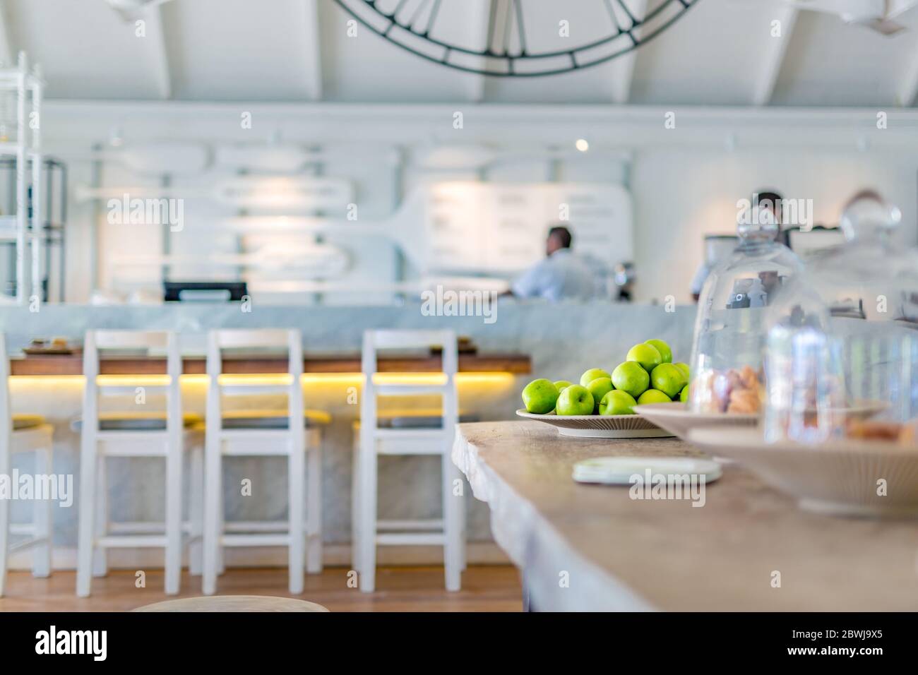 Elegante caffè bianco interno con mele verdi e croissant sotto il vetro. Caffetteria di lusso, tavolo sedie, elementi di design bianchi Foto Stock