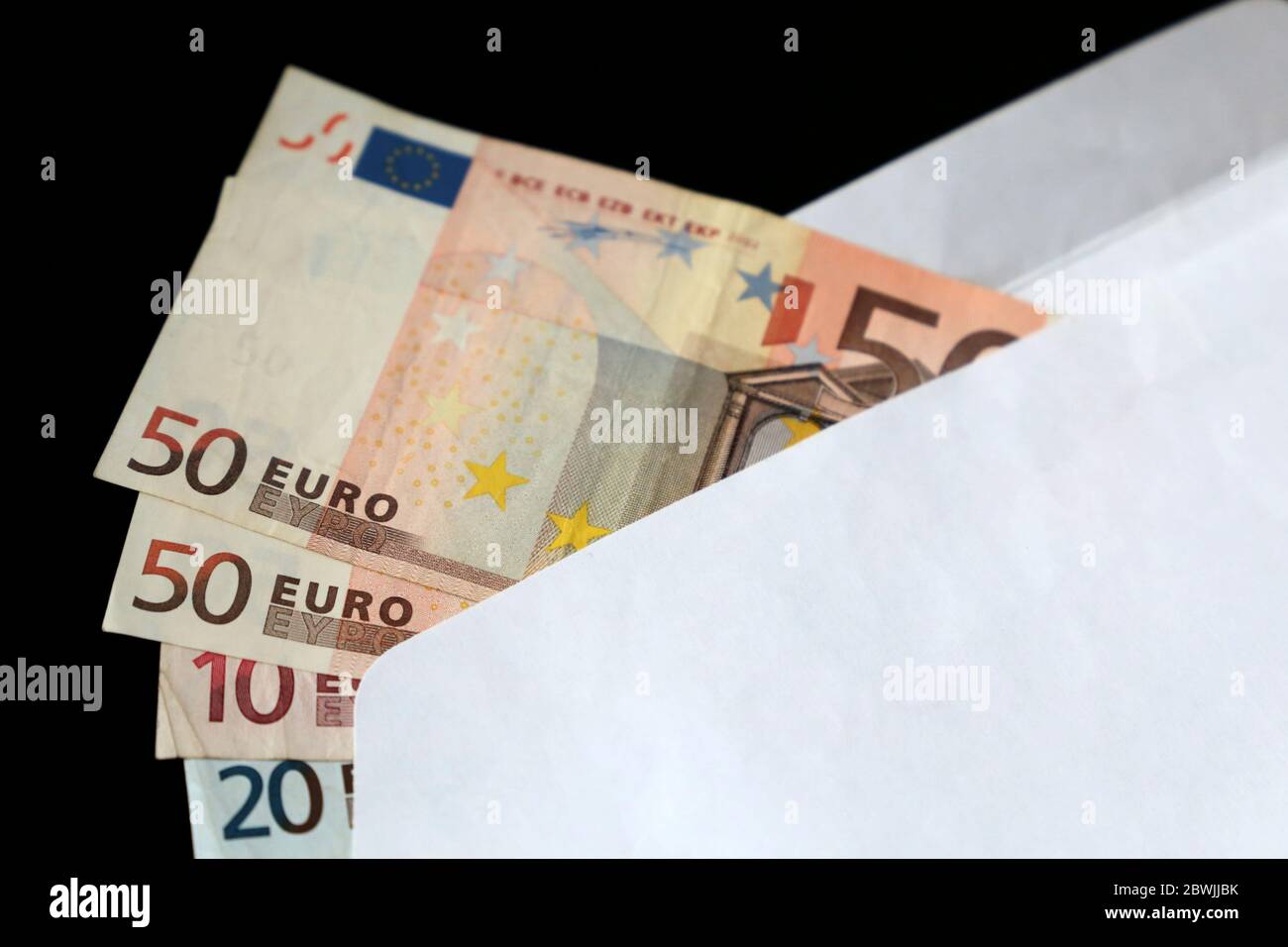 Bollette in euro in busta bianca su sfondo nero. Reddito, bonus o concetto di tangente Foto Stock
