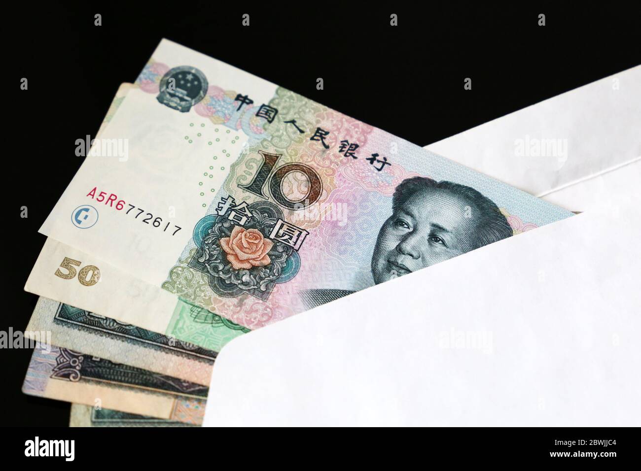 Yuan bollette in busta bianca su sfondo nero. Economia cinese, reddito, bonus o concetto di tangente Foto Stock
