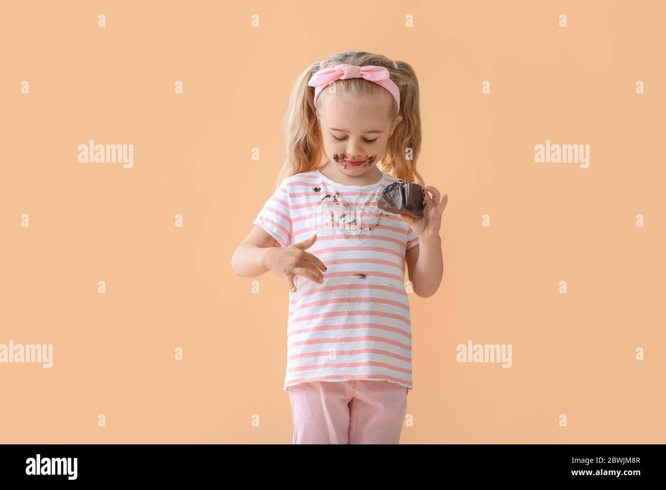 Bambina in vestiti sporchi mangiare torta di cioccolato su sfondo a colori Foto Stock