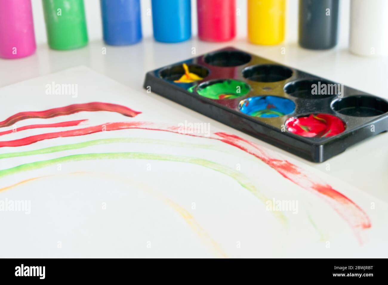Carta bianca con disegno di un bambino fatta di vernice colorata con diversi contenitori di vernice tempera e una tazza di plastica con acqua e pennelli all'interno Foto Stock