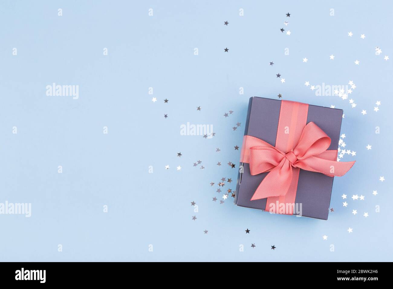 Confezione regalo o regalo e stelle confetti su un tavolo blu dall'alto. Composizione piatta per compleanno, giorno delle madri o matrimonio. Foto Stock