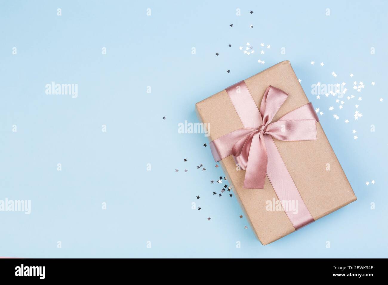 Confezione regalo o regalo e stelle confetti su un tavolo blu dall'alto. Composizione piatta per compleanno, giorno delle madri o matrimonio. Foto Stock