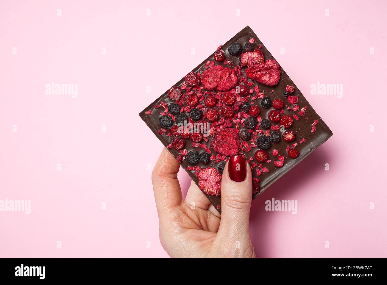 tenere a mano il cioccolato fatto in casa con le bacche su sfondo rosa. Foto Stock