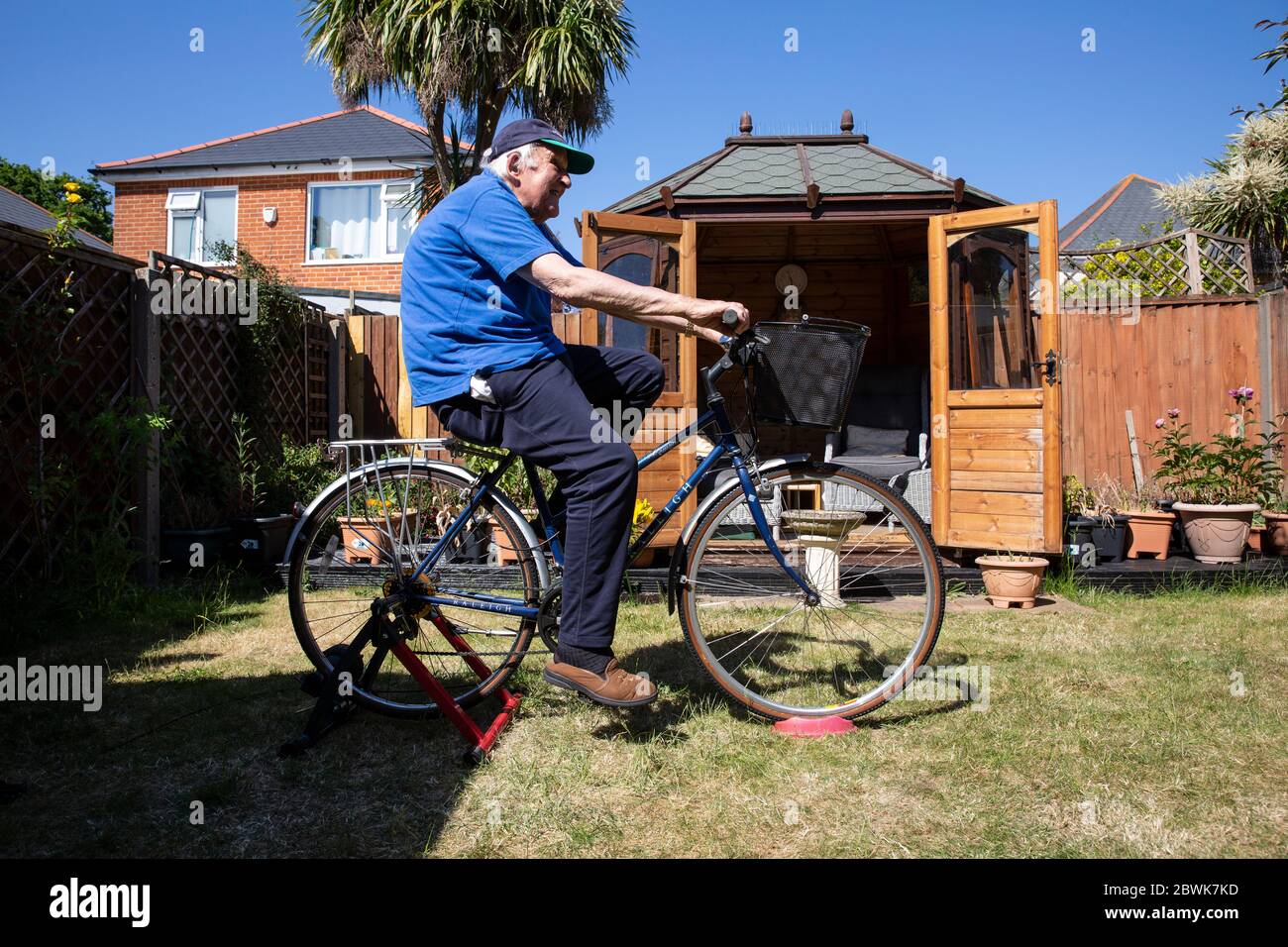 L'uomo anziano nei suoi anni 80 che tiene la forma su un addestratore della bicicletta si trova nel loro giardino posteriore durante il lockdown del coronavirus, Inghilterra sudoccidentale, Regno Unito Foto Stock