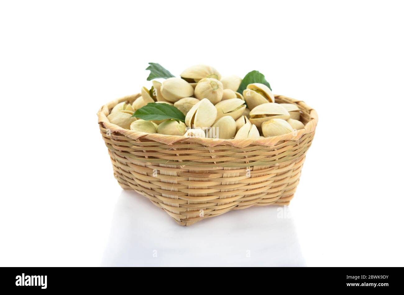 Pistacchio e foglia verde in cesto di bambù isolato su sfondo bianco Foto Stock