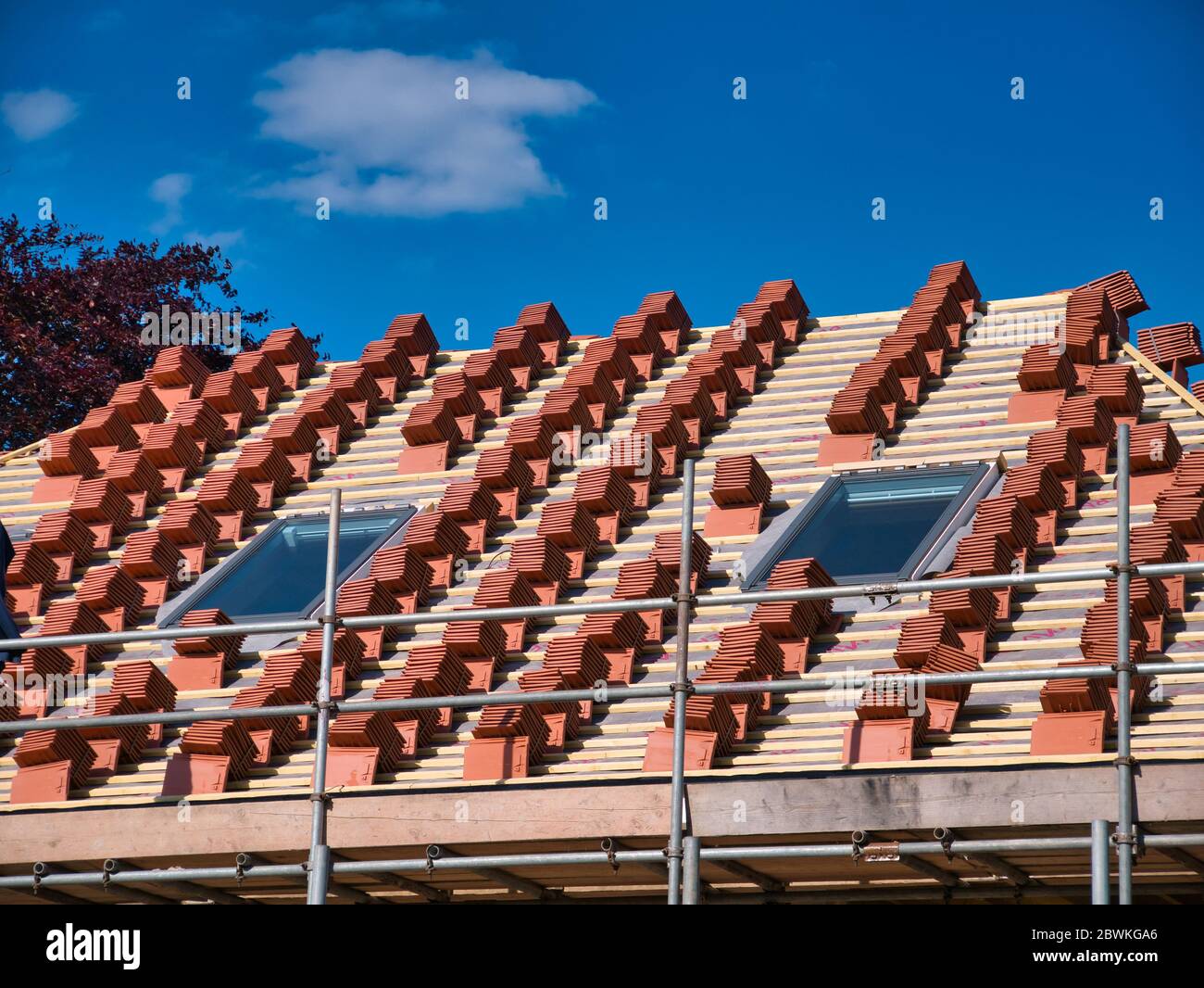 Un tetto di casa in costruzione, che mostra pile di piastrelle di terracotta pronte per essere calzate su listelli di legno. Una giornata di sole con un cielo blu. Foto Stock