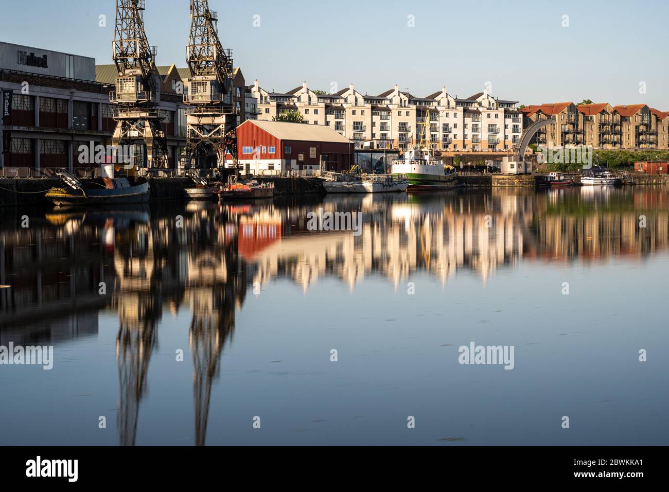 Bristol, Inghilterra, Regno Unito - 25 maggio 2020: La luce del mattino splende sulle gru portuali, i magazzini, le barche storiche e i moderni edifici di appartamenti sul posto di Bristol Foto Stock