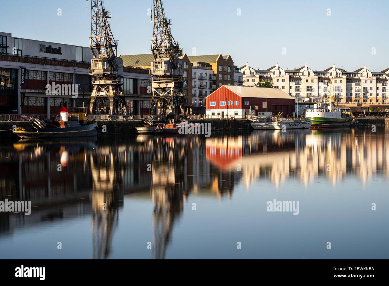 Bristol, Inghilterra, Regno Unito - 25 maggio 2020: La luce del mattino splende sulle gru portuali, i magazzini, le barche storiche e i moderni edifici di appartamenti sul posto di Bristol Foto Stock