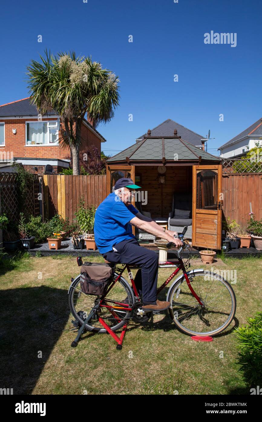 L'uomo anziano nei suoi anni 80 che tiene la forma su un addestratore della bicicletta si trova nel loro giardino posteriore durante il lockdown del coronavirus, Inghilterra sudoccidentale, Regno Unito Foto Stock