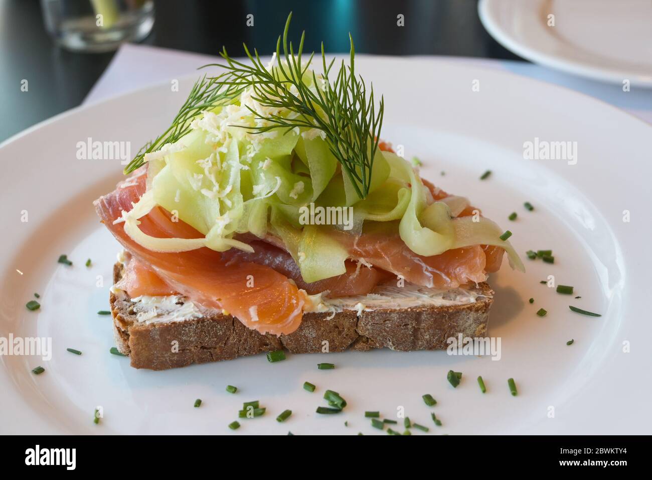 pane integrale con salmone, cetriolo, fiocchi di rafano e guarnitura di aneto servito su un piatto bianco, fuoco selezionato, profondità di campo stretta Foto Stock