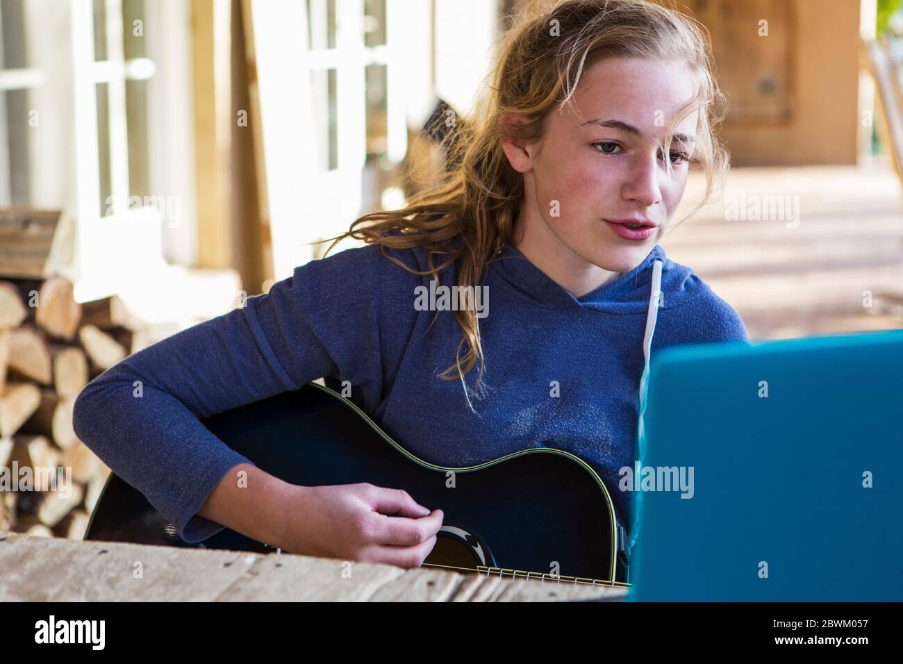 Una ragazza adolescente che guarda il laptop, cantando e suonando la chitarra Foto Stock