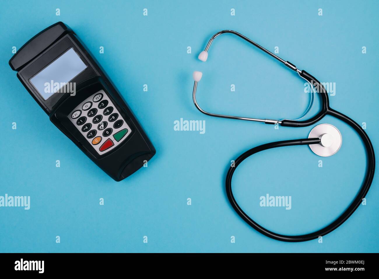 costo e pagamento per trattamento medico o concetto di copay, sopra shot di stetoscopio e lettore di carte di credito su sfondo blu scrivania Foto Stock