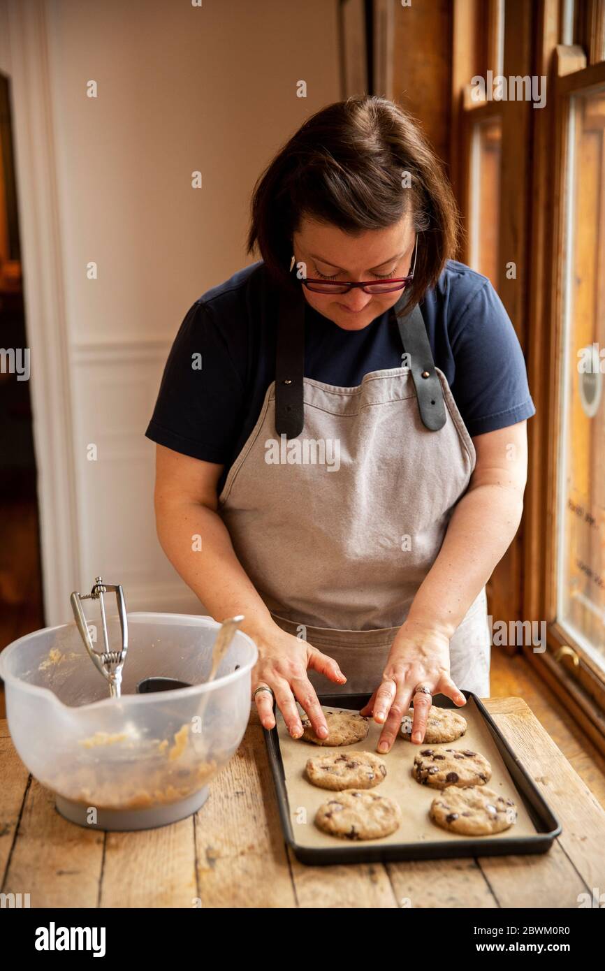 Donna che indossa bicchieri e grembiule in piedi a tavola di legno, cottura biscotti chip cioccolato. Foto Stock