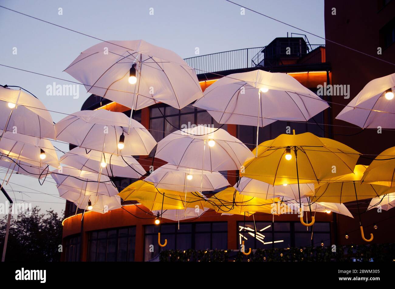 Strada cittadina decorata con ombrelloni e luci. Architettura design esterno in serata. Foto Stock