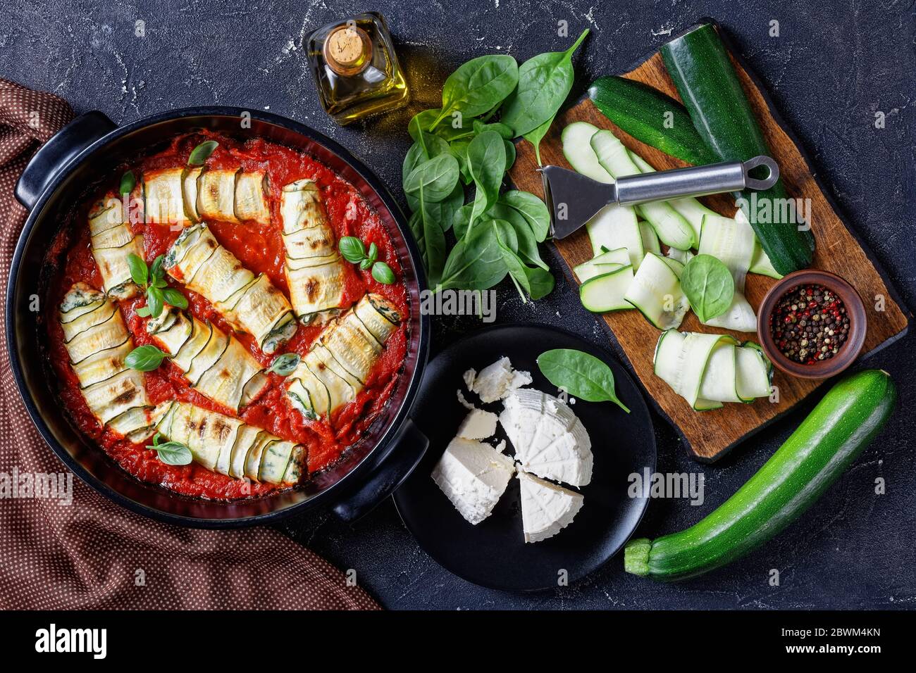 Involtini di zucchine ripieni di ricotta fresca italiana con spinaci e foglie di basilico cotti in salsa di pomodoro serviti su una panetteria nera Foto Stock