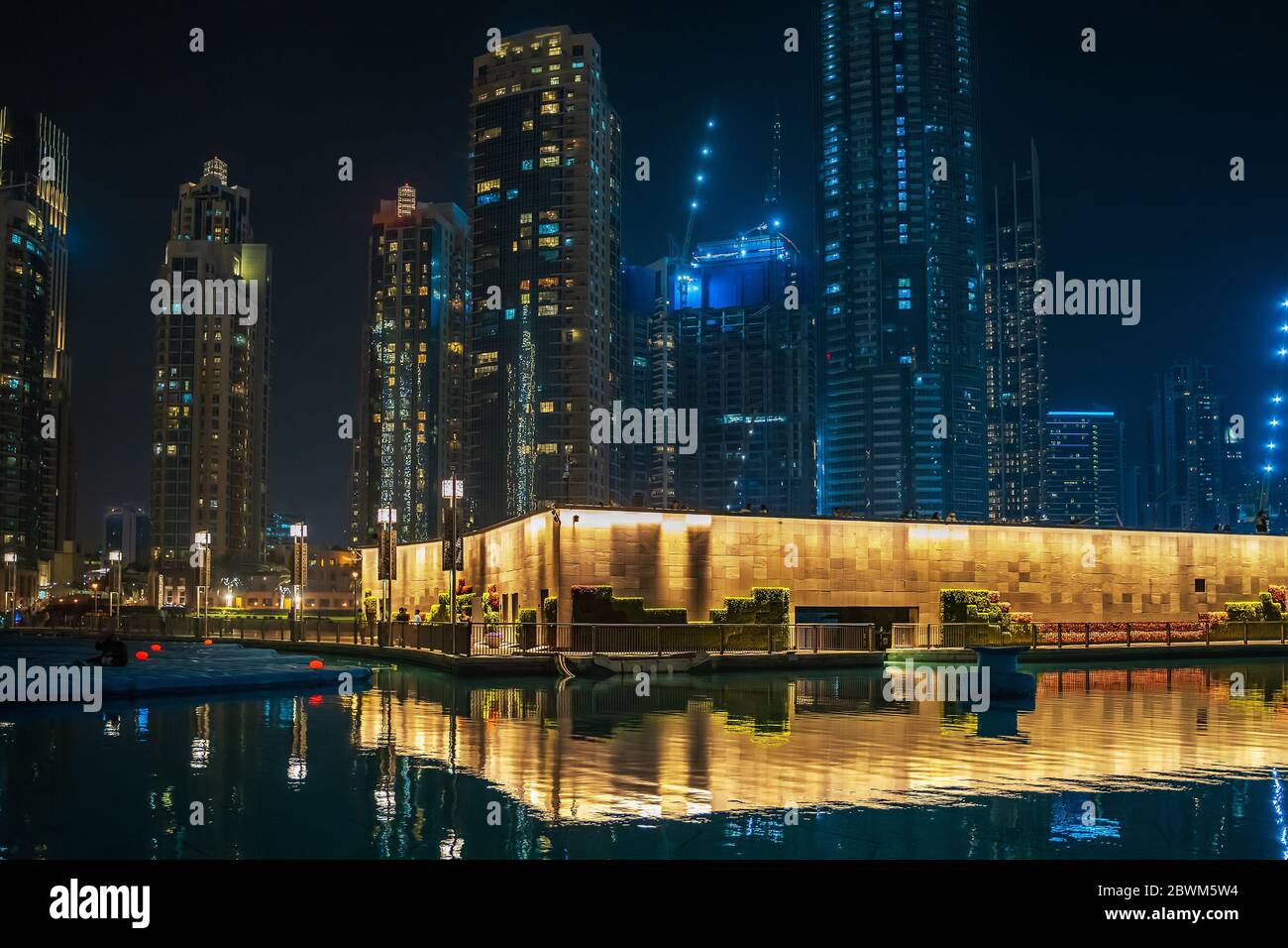 Piscina con riflessi e alti edifici illuminati di notte a Dubai, Emirati Arabi Uniti. Foto Stock