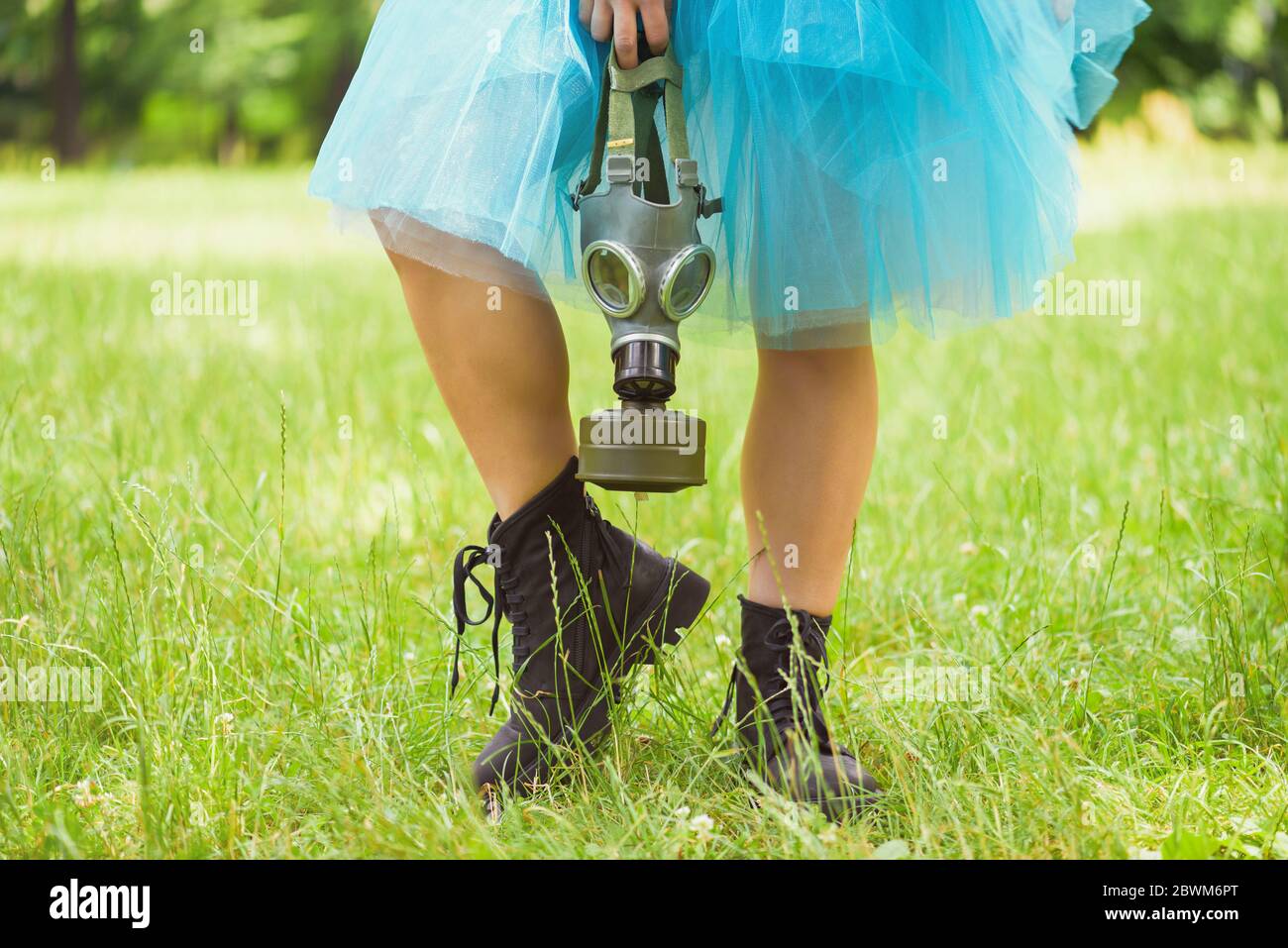 Donna in gonna blu con maschera a gas in piedi su erba verde in un parco. Protezione ambientale, rischio biologico e concetto ecologico Foto Stock