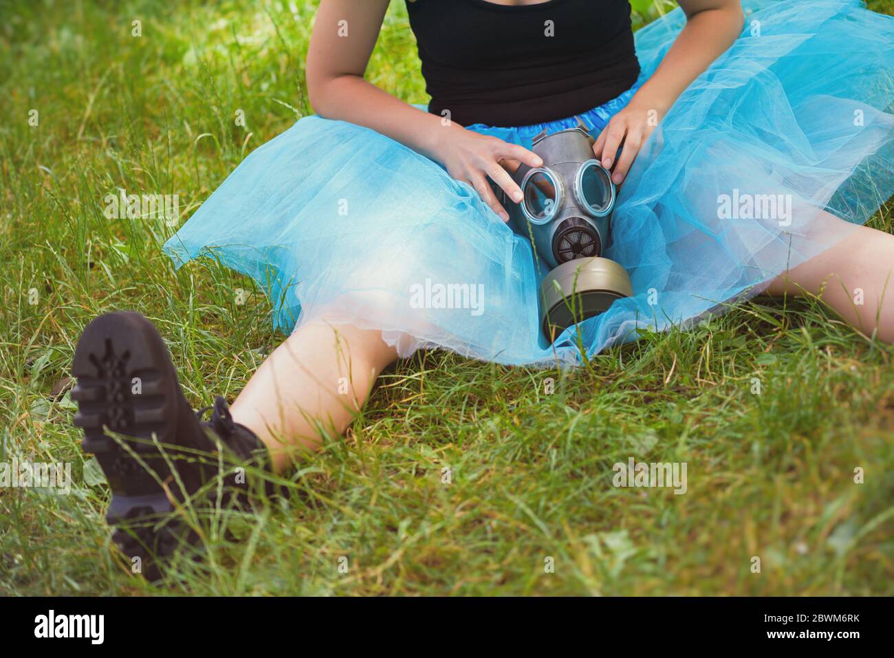 Donna in gonna blu con maschera a gas si siede su erba verde. Protezione ambientale, rischio biologico e concetto ecologico Foto Stock