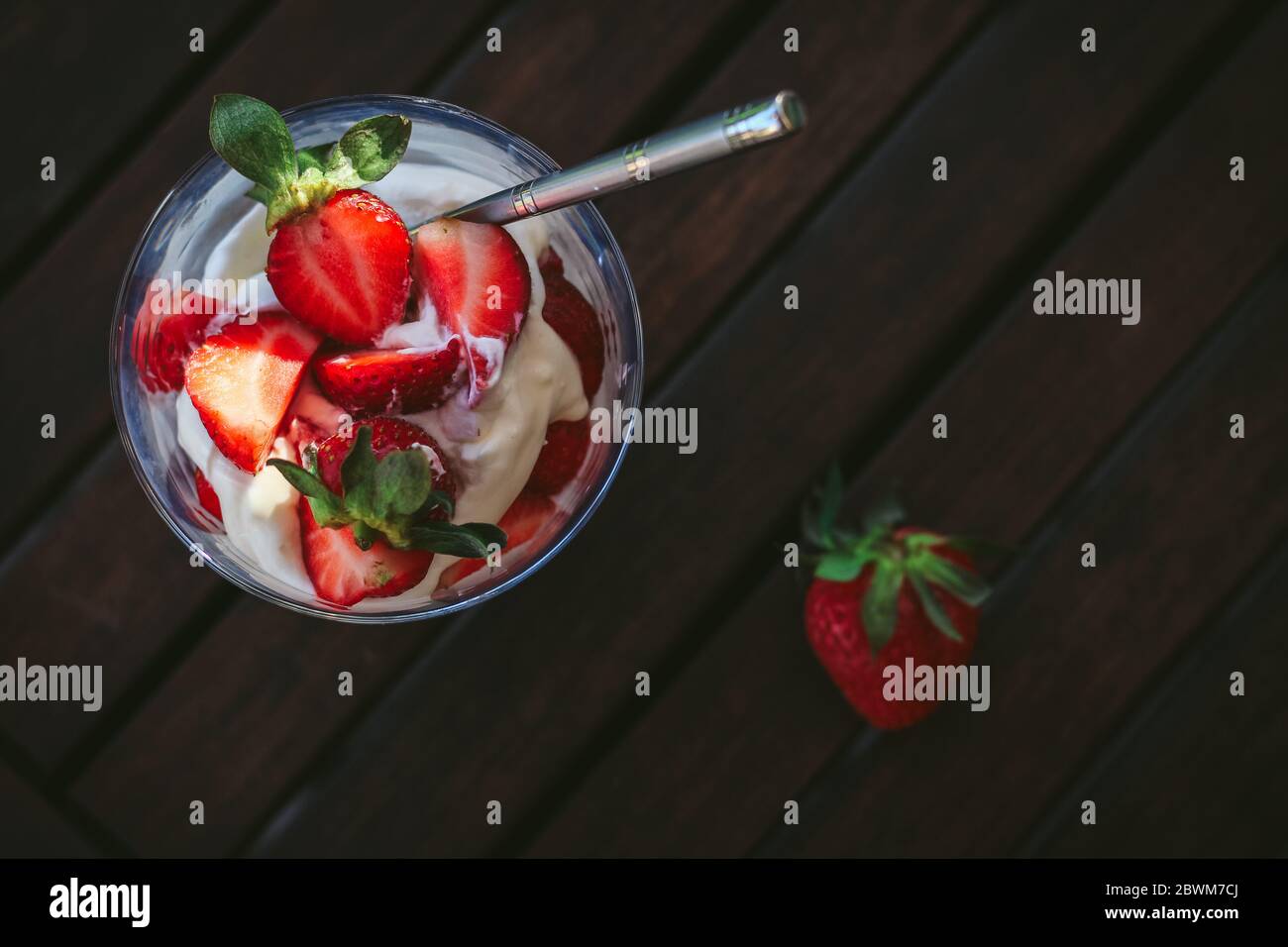 Dessert estivo in vetro con crema di mascarpone e fragole su un tavolo da giardino scuro, girato dall'alto Foto Stock