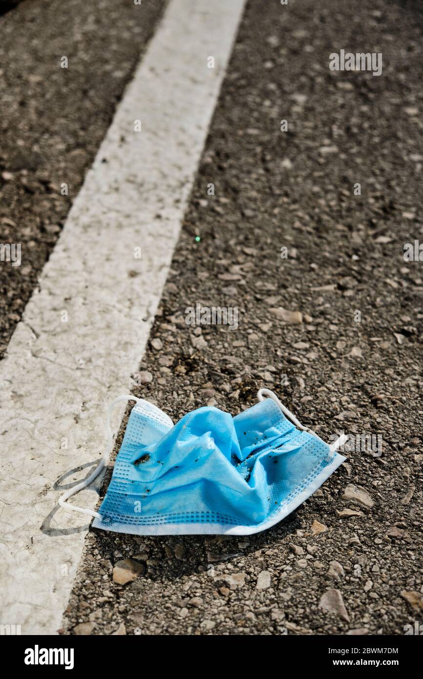 primo piano di una maschera chirurgica blu utilizzata gettata sull'asfalto di una strada, un parcheggio o una strada Foto Stock