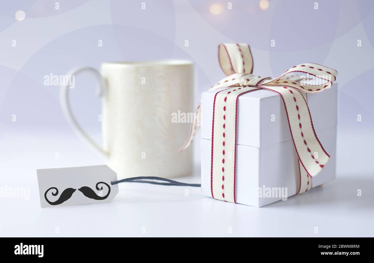 Tazza di caffè del mattino, confezione regalo confezionata, etichetta regalo con l'icona dei baffi su sfondo chiaro con bokeh. Giorno dei padri, concetto di compleanno Foto Stock