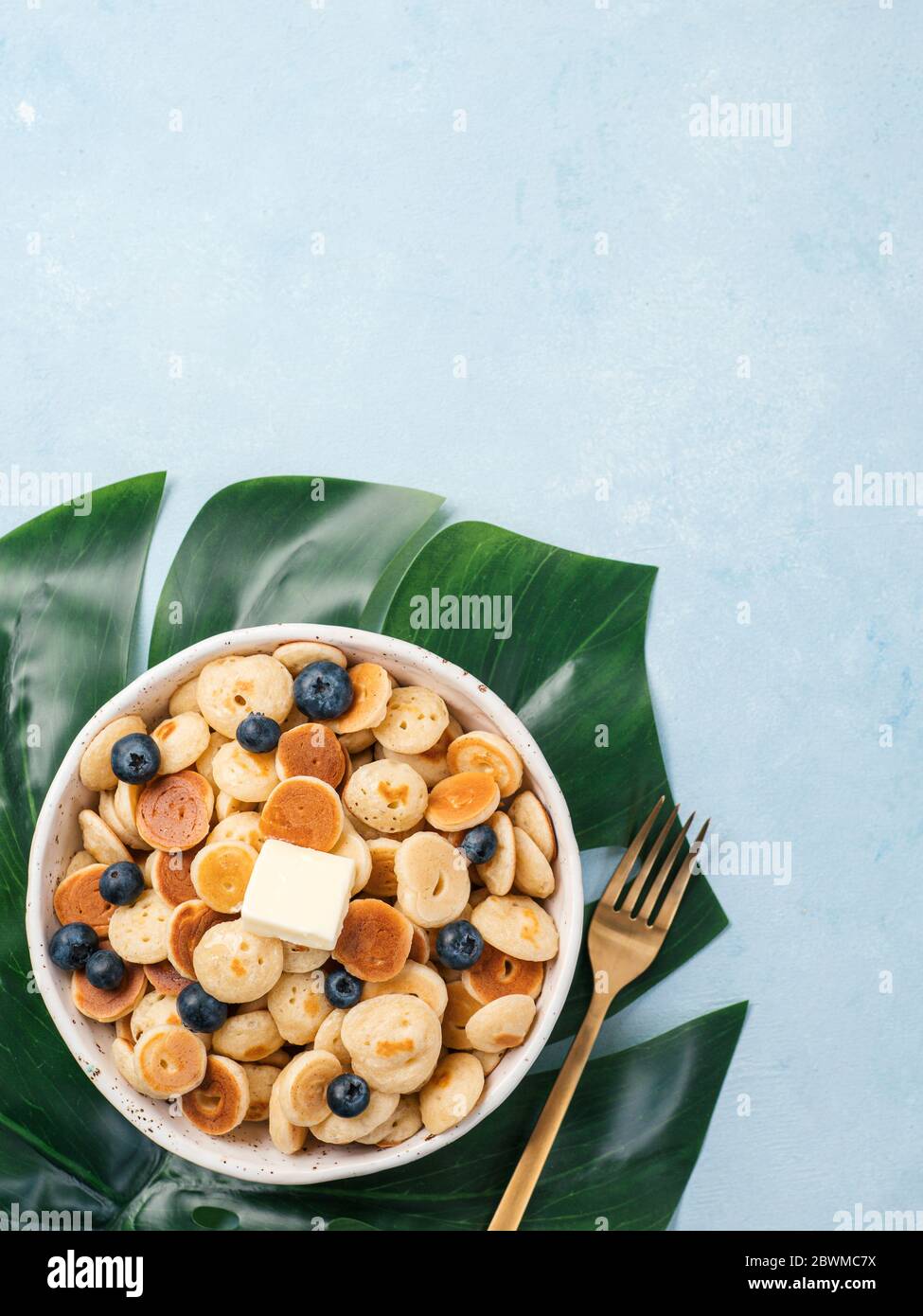 Cibo alla moda - cereali pancake. Un mucchio di mini frittelle di cereali in boul su sfondo blu. Copia spazio a sinistra per il testo. Vista dall'alto o in piano. Verticale. Foto Stock