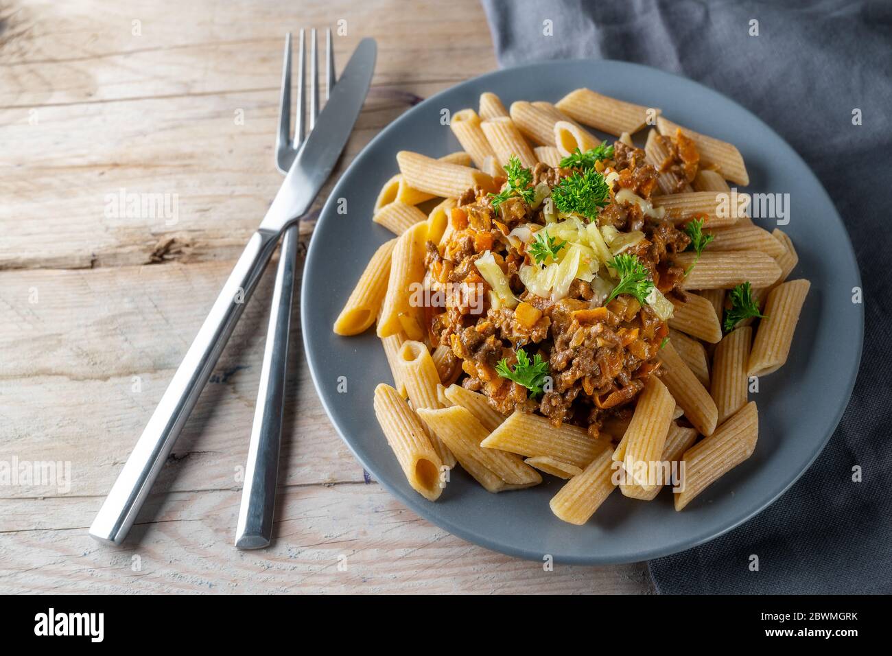 tagliatelle di penne integrali con salsa di carne macinata e carote, parmigiano e prezzemolo, posate su un rustico tavolo di legno, spazio copia, se Foto Stock