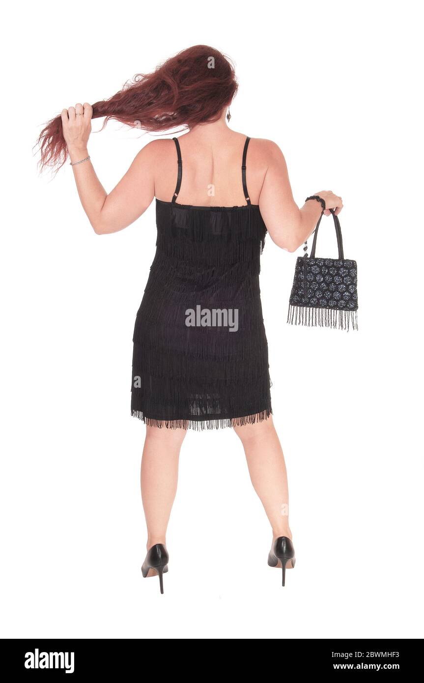Una bella donna in piedi in un vestito nero dalla schiena con i suoi lunghi capelli rossi, isolato per sfondo bianco Foto Stock