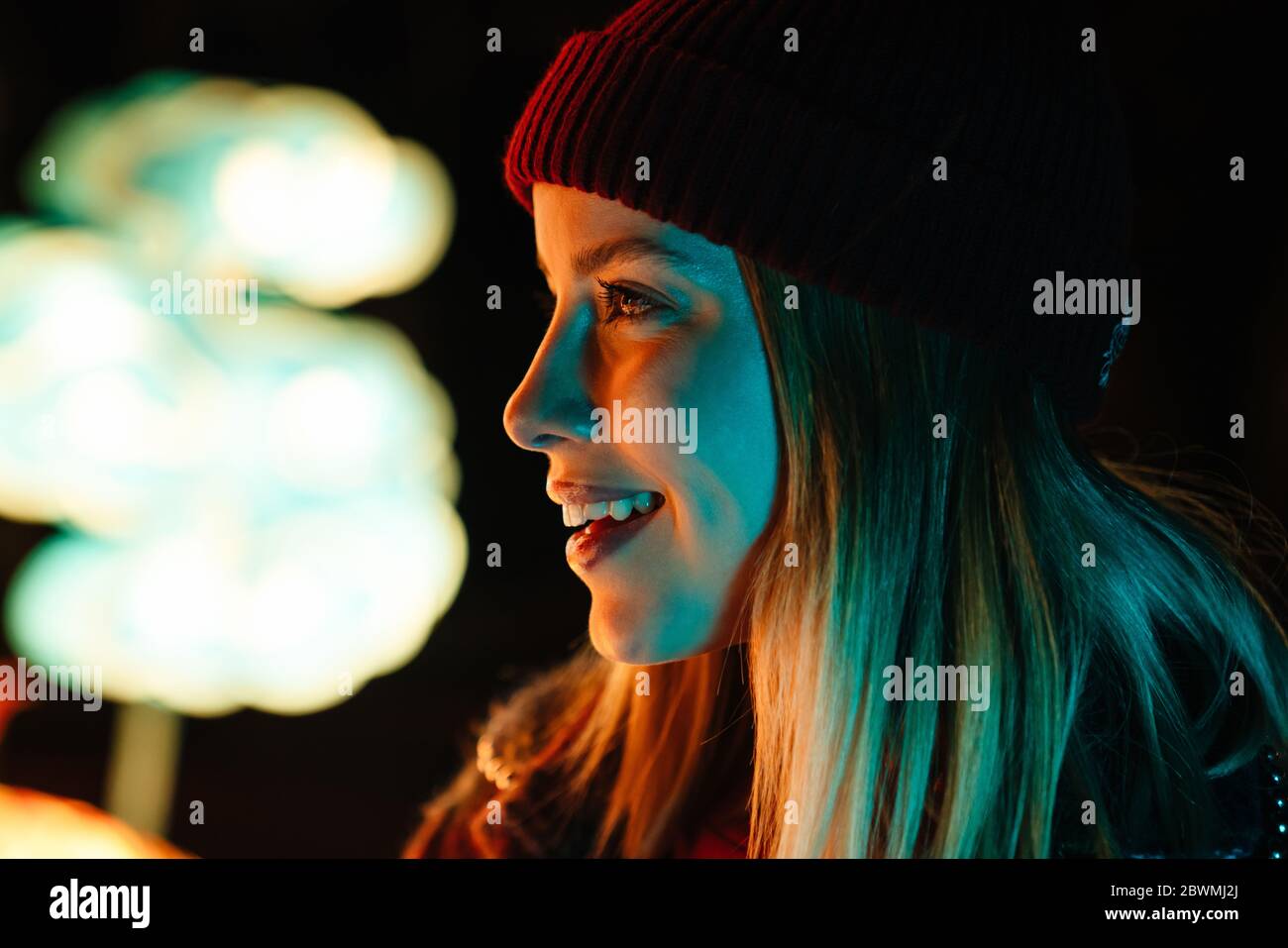 Foto di una bella gioiosa donna sorridente e che guarda da parte mentre si cammina al parco con luci al neon Foto Stock