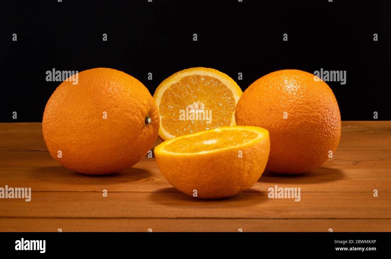 Metà fresca e succosa e fetta di frutta arancione su un tavolo di legno su sfondo nero. Foto Stock