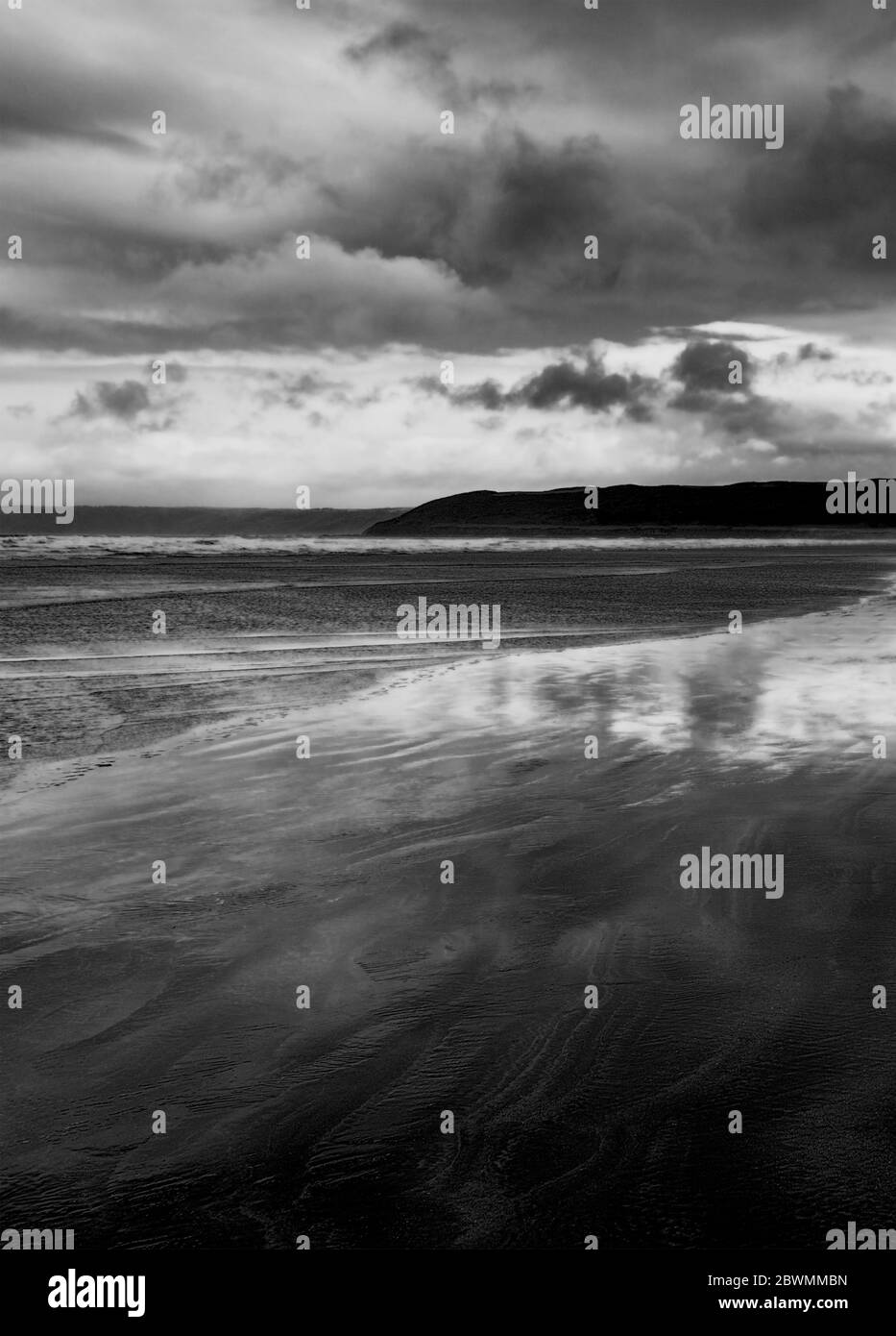 Immagine in bianco e nero di una spiaggia sabbiosa illuminata dalla luna di notte, nuvole sopra un promontorio lontano, adatto per una copertina del libro Foto Stock