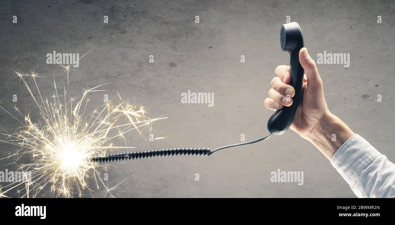 L'uomo d'affari tiene un telefono con un cavo telefonico che brucia. Concetto per l'aiuto telefonico di emergenza o hotline. Foto Stock