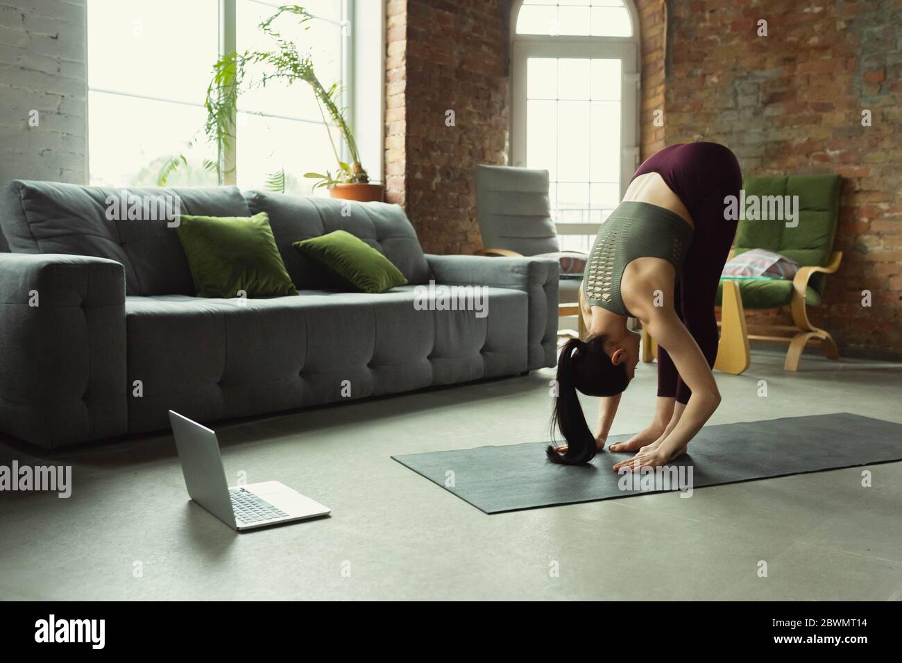 Forte. Sportivo bella giovane donna che prende lezioni professionali di yoga online e pratica a casa. Concetto di stile di vita sano, benessere, alla ricerca di un nuovo hobby. Flessibile e motivato. Foto Stock