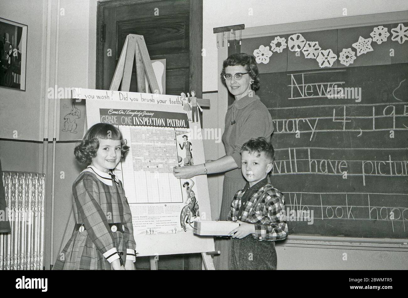 Istruzione negli Stati Uniti negli anni '50 – in una classe un insegnante e due alunni si trovano di fronte a una lavagna bianca con una carta sull'igiene personale. Le domande 'did lavate?' e 'fai spazzolare i denti?' fanno parte di questo schema diretto agli studenti di grado uno nella scuola elementare. Ci sono notizie scritte a mano sulla lavagna dietro di loro. Foto Stock