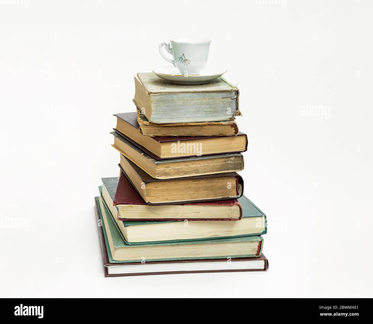 una pila di vecchi libri. Al piano superiore si trova un'elegante tazza di caffè e un piatto. Su sfondo bianco. Foto Stock