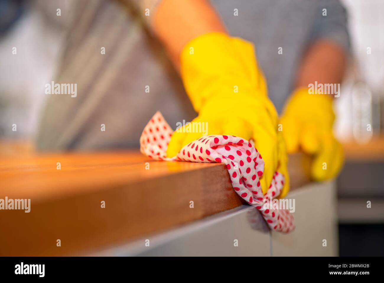 Persona con guanti di gomma gialla salviette con un panno sopra un piano di lavoro in cucina Foto Stock