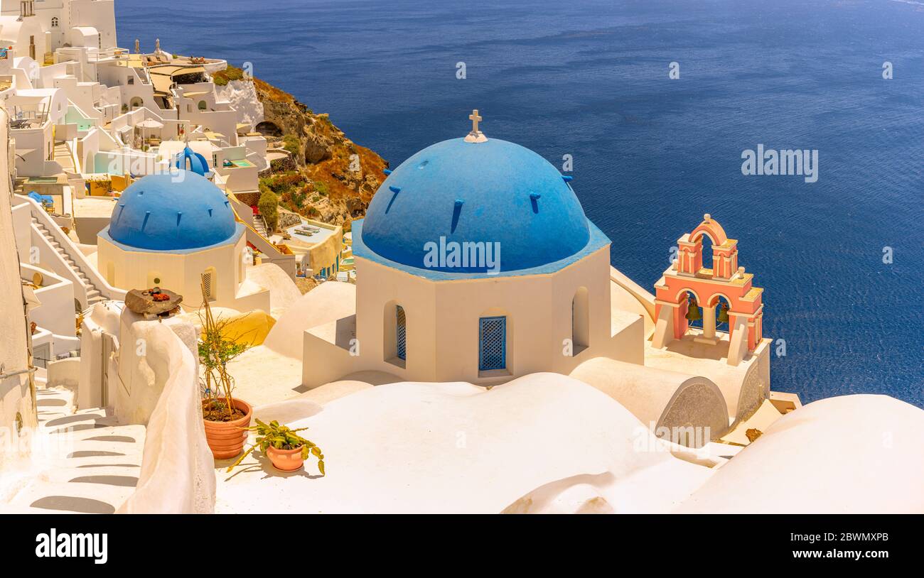 Le splendide e iconiche cupole blu di Santorini, un'isola greca, si affacciano sul Mar Egeo e sul contrastante campanile color pesca. Foto Stock