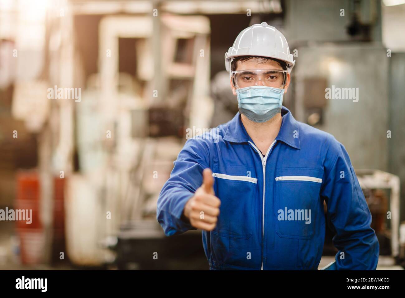 Operatore che indossa una visiera protettiva o una maschera monouso durante il lavoro in fabbrica per prevenire l'inquinamento da Coronavirus (Covid-19) o polvere d'aria in fabbrica Foto Stock