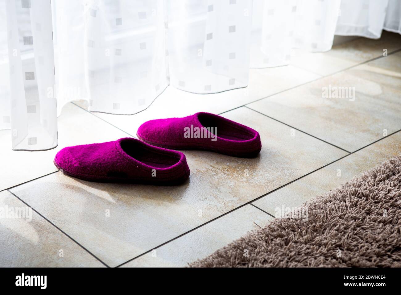 primo piano di pantofole viola sul pavimento da una tenda bianca Foto Stock