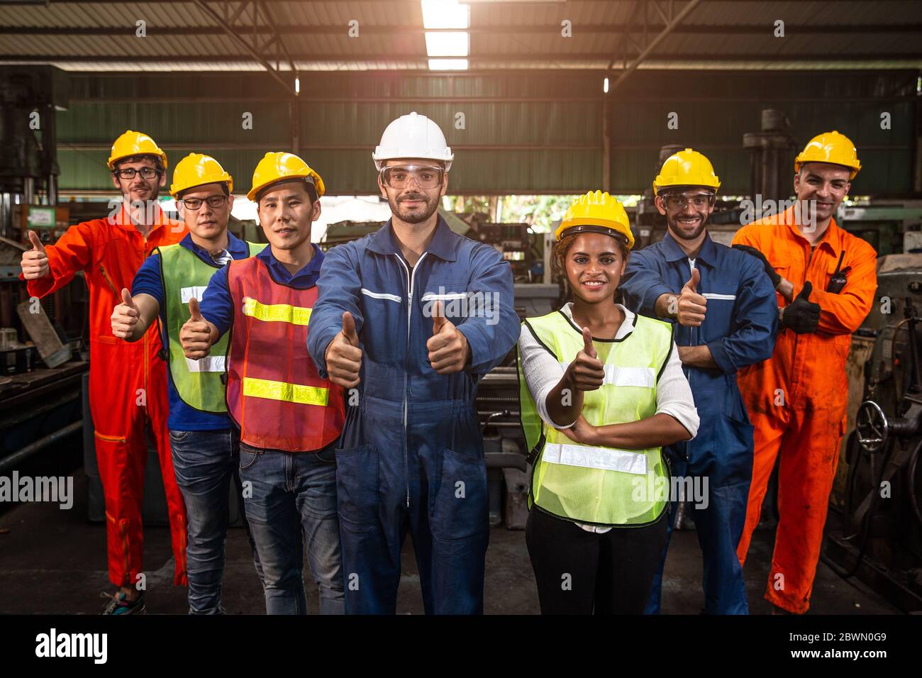 Gruppo di Team Worker mix gara godere di lavorare in fabbrica pesante stare insieme sorridendo felice mano mostra pollici su ampio banner. Foto Stock