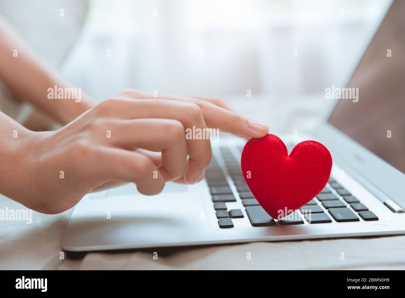 Mano che tocca cuore rosso sulla tastiera del laptop per flirt amore chat o amante di testo in linea Messenger per trovare la coppia di date durante soggiorno a casa Coronavirus pandem Foto Stock