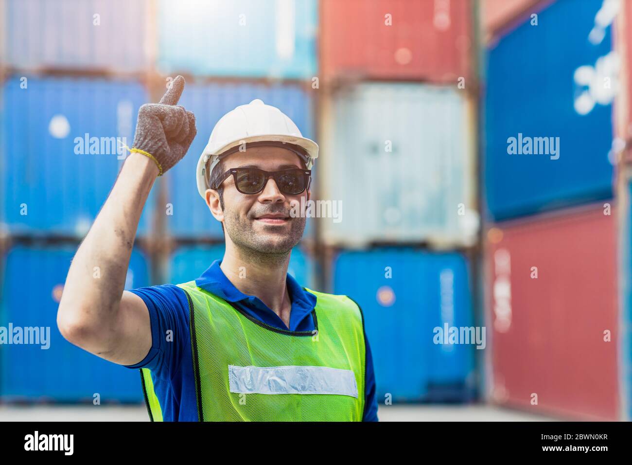 Ritratto di successo caposquadra di trasporto lavoratore latino di lavoro nel porto di carico per l'importazione merci di esportazione in piedi sorriso con occhiali da sole. Foto Stock