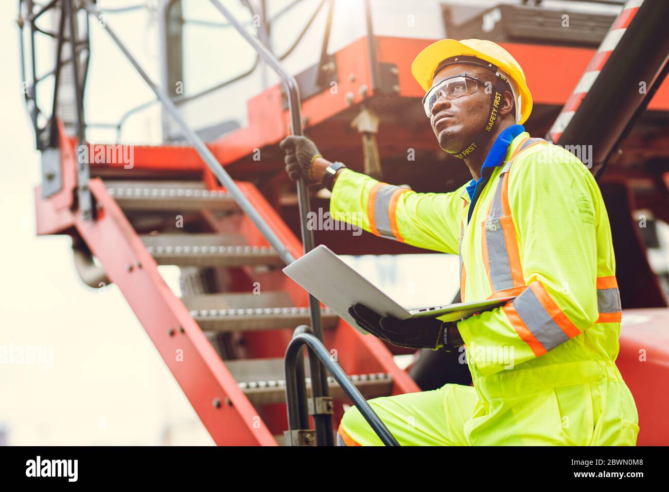 Il caposquadra del personale nero africano intende lavorare caricando il lavoratore usando il computer portatile per controllare la spedizione del carico nel deposito logistico. Foto Stock