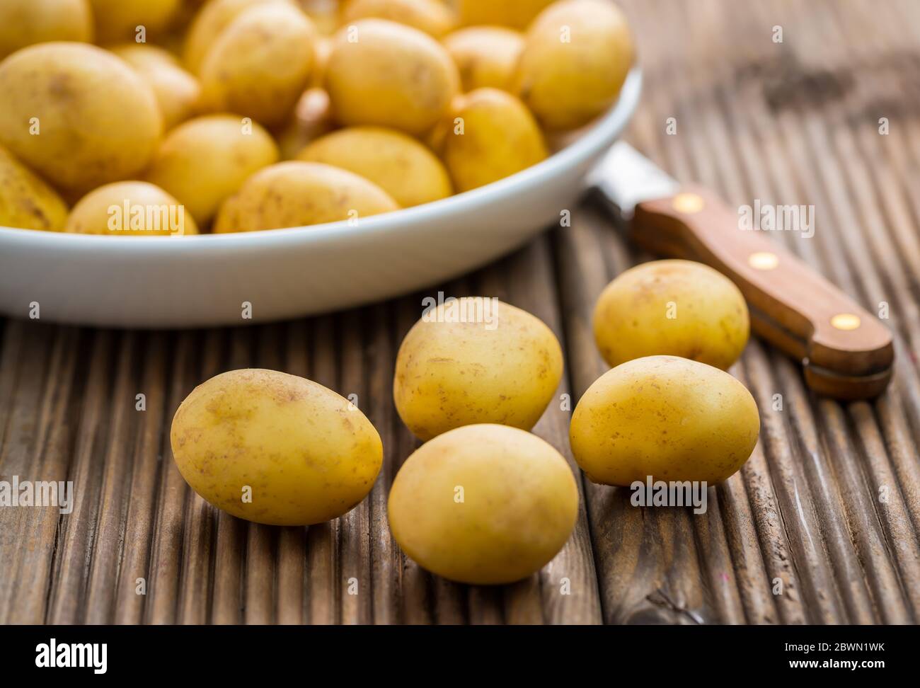 Patate biologiche fresche in ciotola con coltello su fondo di legno Foto Stock