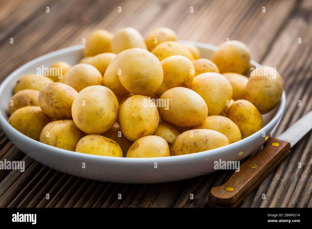 Patate biologiche fresche in ciotola con coltello su fondo di legno Foto Stock