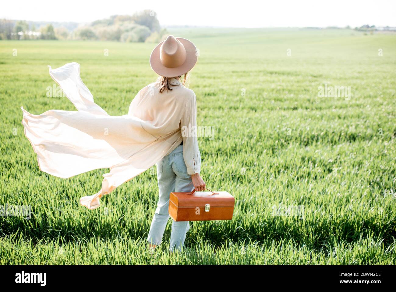 Ritratto di una donna elegante che cammina con la borsa sul campo verde, godendo la natura in primavera. Concetto di benessere e stile di vita spensierato sulla natura Foto Stock