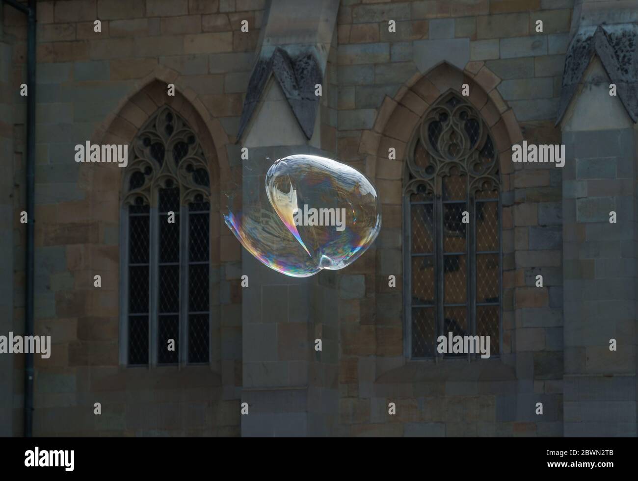 Bolla di sapone a forma di cuore esplode come concetto di qualcosa che finisce improvvisamente, muro di una chiesa edificio come sfondo Foto Stock