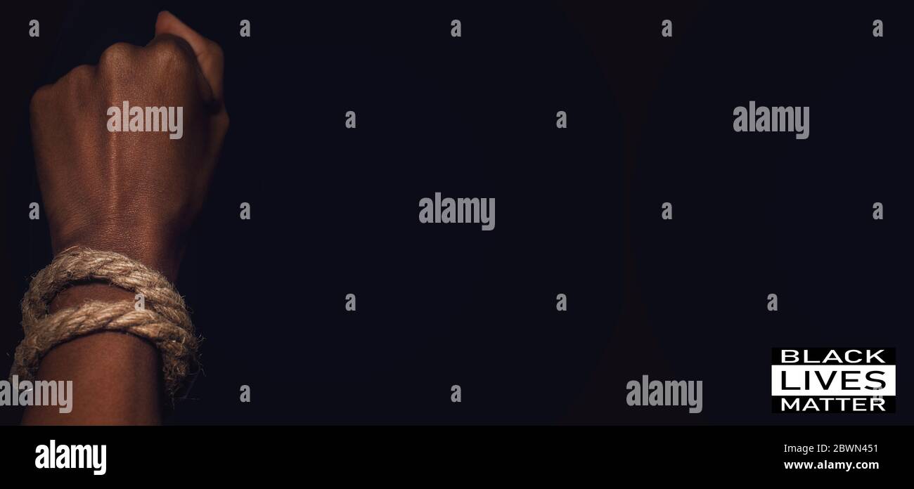 Closeup scuro di mano donna nera pugno legato da corda. Gesto di forza e di potenza. Messa a fuoco selettiva sulla corda. Concetto di uguaglianza di genere e razziale. Foto Stock