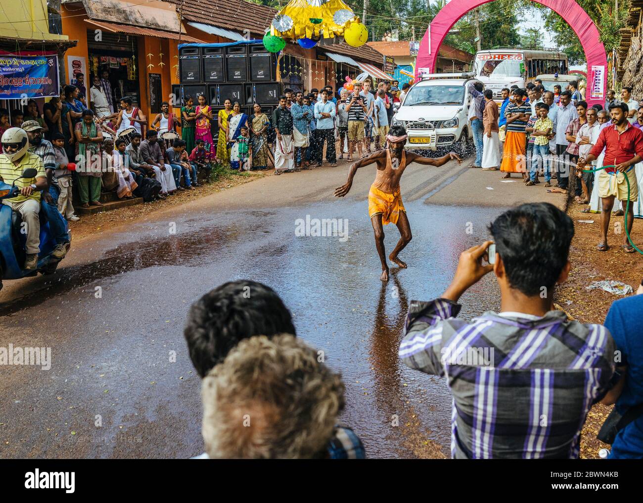 L'uomo balla in strada e fa oscillare un pipistrello per schioccare colorati palloncini d'acqua attaccati a una piramide simbolica oscillata da una corda e una puleggia, mentre i batteristi tengono il passo e i partecipanti giocosi schlashe Foto Stock